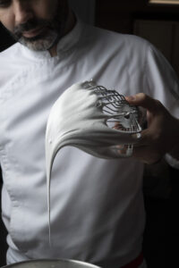 Chef Dominique holding a whisk with meringue